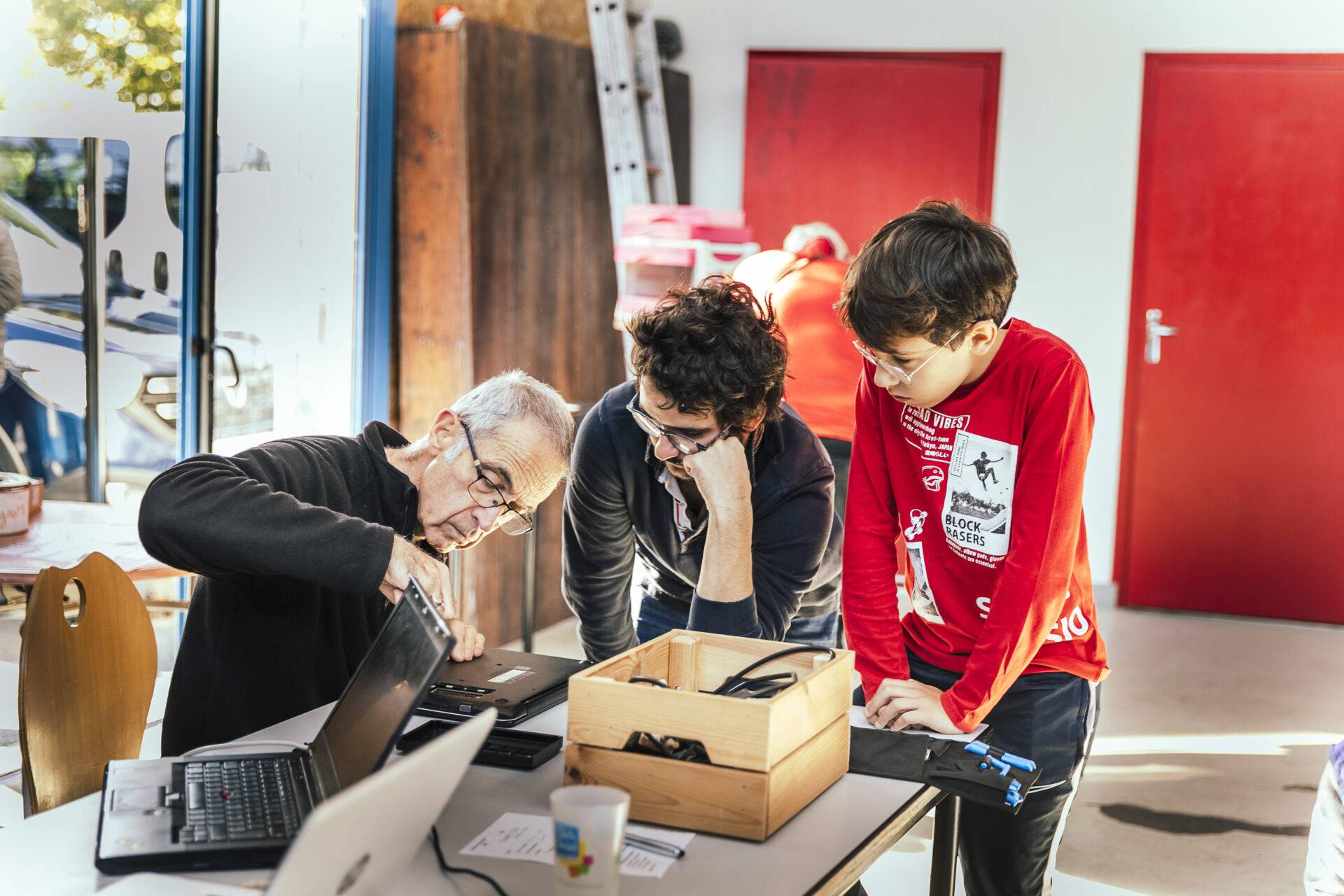 image d'illustration : un bénévole répare un ordinateur avec l'aide d'un homme et d'un enfant. contexte intergénérationnel